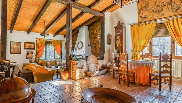 A rustic room with exposed wooden beams, a stone fireplace, a dining table with yellow curtains, and a large metal basin. - Pet friendly home in Valverde de Leganés (Valverde de Leganés)