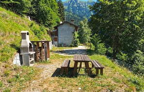 Un chalet de montagne rustique, doté d’une cheminée en pierre, d’un banc en bois et d’une table de pique-nique.