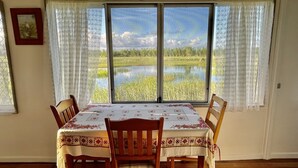 Una zona de menjador amb una taula preparada per a quatre, una finestra que ofereix vistes a un llac i vegetació, i un quadre al mur.