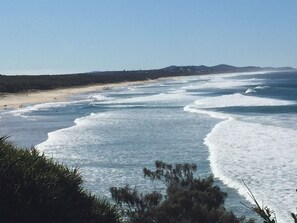 A coastal beach scene with waves, a sandy shore, and distant hills.