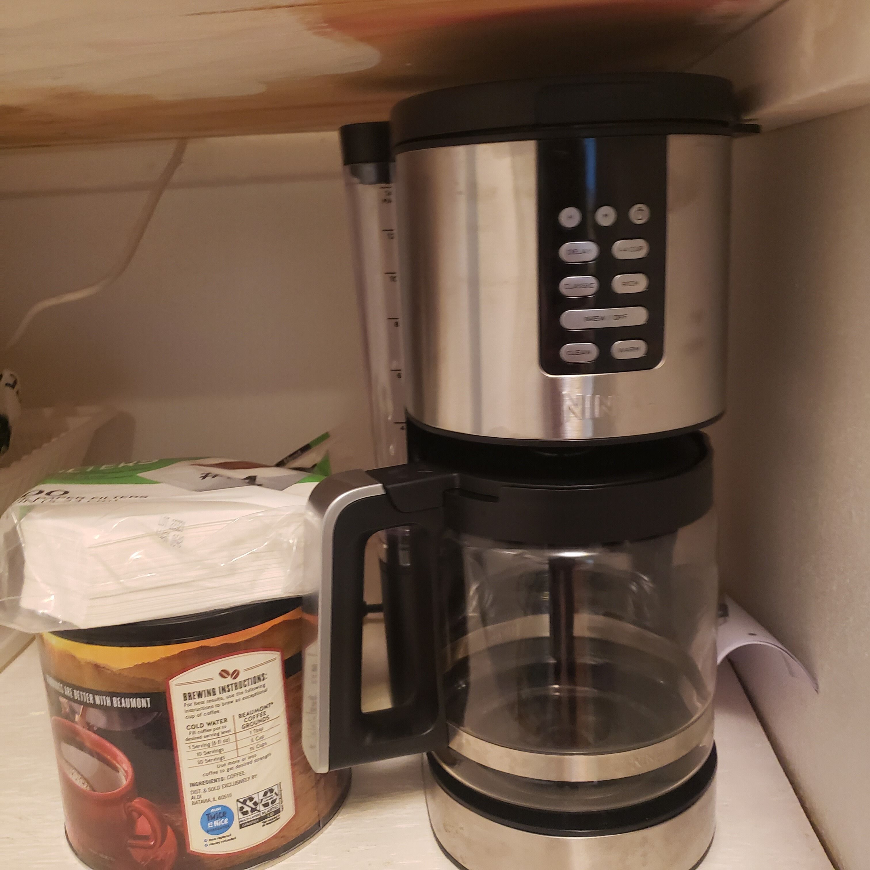 A coffee maker with a glass carafe and a coffee pod on a shelf.