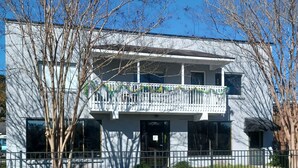 A two-story building with a balcony, a fenced yard, and a clear blue sky. - Bon Aire Apartment is in downtown Mobile on the Mardi Gras Parade Route
 (Mobile)