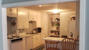 A kitchen with white cabinets, a stove, and a microwave. There are two wooden chairs and a small island with a sink. - Bon Aire Apartment is in downtown Mobile on the Mardi Gras Parade Route
 (Mobile)