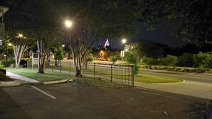 A nighttime view of a residential area with a well-lit street, a gated entrance, and a building with illuminated signage. - Bon Aire Apartment is in downtown Mobile on the Mardi Gras Parade Route
 (Mobile)