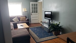 A living room with a sofa, coffee table, TV, and a door. - Bon Aire Apartment is in downtown Mobile on the Mardi Gras Parade Route
 (Mobile)