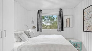 Une chambre à coucher avec un lit, une table de chevet, une fenêtre avec des rideaux, un tableau encadré et une petite table.