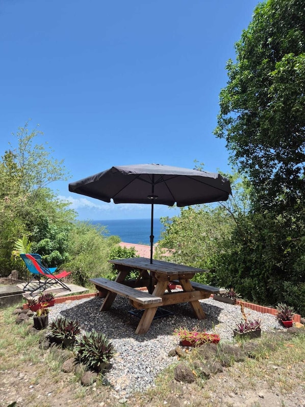 Une table de pique-nique en bois, agrémentée d’un parasol, entourée de gravier et de plantes en pot, et offrant une vue panoramique.