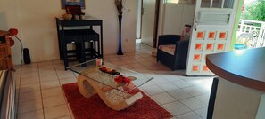 Una habitación con una mesa de centro de vidrio, un tapete rojo, una silla negra y una puerta blanca con diseños geométricos anaranjados.