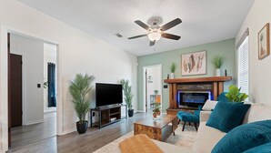 A living room with a fireplace, a ceiling fan, and a television. - 🌟Downtown Pensacola Getaway!🌟 Fenced in yard for fur babies! (Pensacola)