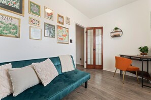A living room with a teal sofa, a wooden dining table with an orange chair, and a bookshelf.