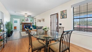 A dining area with a glass table and chairs, a fireplace, and a view of the outdoors through large windows. - 🌟Downtown Pensacola Getaway!🌟 Fenced in yard for fur babies! (Pensacola)