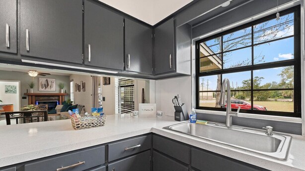 A modern kitchen with dark cabinets, a white countertop, and a large window with a view of the outside. - 🌟Downtown Pensacola Getaway!🌟 Fenced in yard for fur babies! (Pensacola)