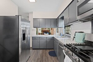 A modern kitchen with grey cabinets, a stainless steel refrigerator, a gas stove, and a microwave.