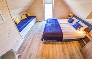 Une petite chambre mansardée avec deux lits, un plancher en bois et une petite fenêtre.