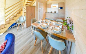 Une cuisine moderne avec des meubles en bois, un coin repas avec une table dressée pour quatre personnes, et un escalier menant à l’étage supérieur.