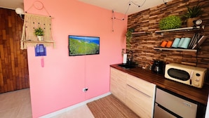 A kitchen with a pink wall, wooden cabinets, a microwave, and a TV mounted on the wall.