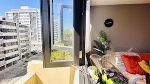 A balcony with a view of high-rise buildings, a small seating area with cushions, and a potted plant.