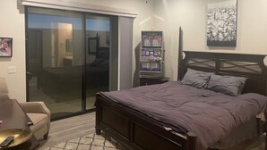 A bedroom with a bed, a ceiling fan, a nightstand with a lamp, a chair, a remote control, and a window with a view. - Colorado River Getaway, Resort Pool, Waterslide & Mountain Views (Fort Mohave)