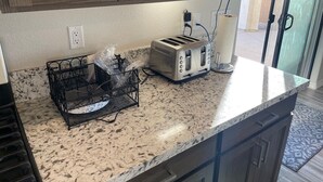A kitchen with granite countertops, a toaster, a basket with utensils, and wooden cabinets. - Colorado River Getaway, Resort Pool, Waterslide & Mountain Views (Fort Mohave)