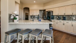 Una cocina con una isla central, taburetes de bar y un refrigerador.