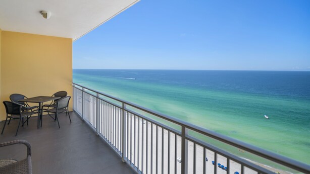A balcony with a view of the ocean, a table with chairs, and a railing.