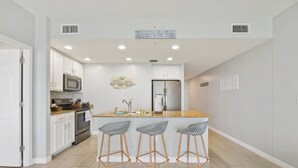 A modern kitchen with white cabinetry, a central island with bar stools, stainless steel appliances, and a 'Welcome to Our Home' sign.