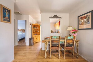 A dining area with a wooden table and chairs, a kitchen in the background, and a hallway leading to a bedroom. - Cozy Casita in Downtown Albuquerque (Albuquerque)