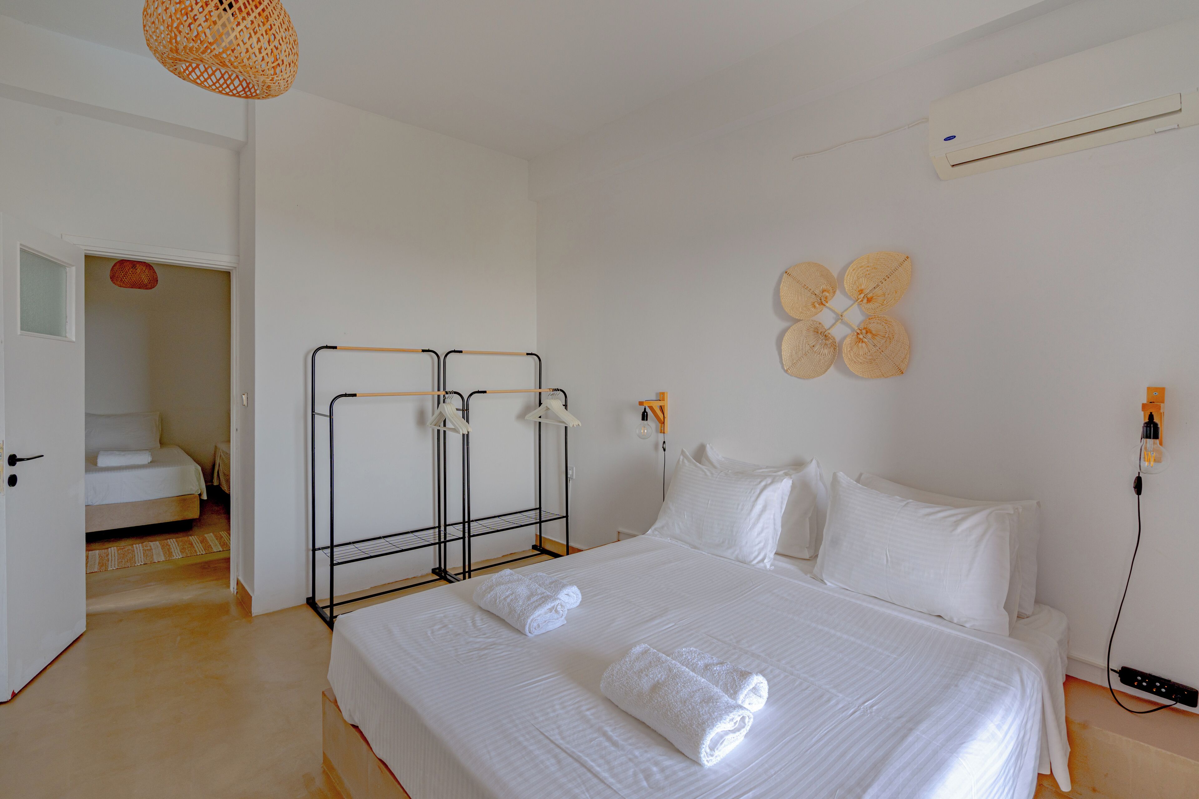 Habitación de hotel con una cama grande, una mesita de noche, aire acondicionado instalado en la pared y una puerta que da a otra habitación.