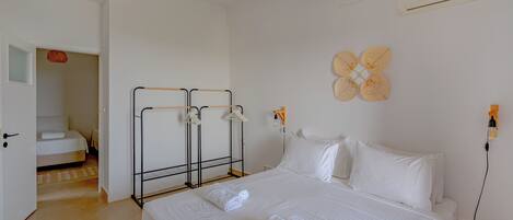 Habitación de hotel con una cama grande, una mesita de noche, aire acondicionado instalado en la pared y una puerta que da a otra habitación.