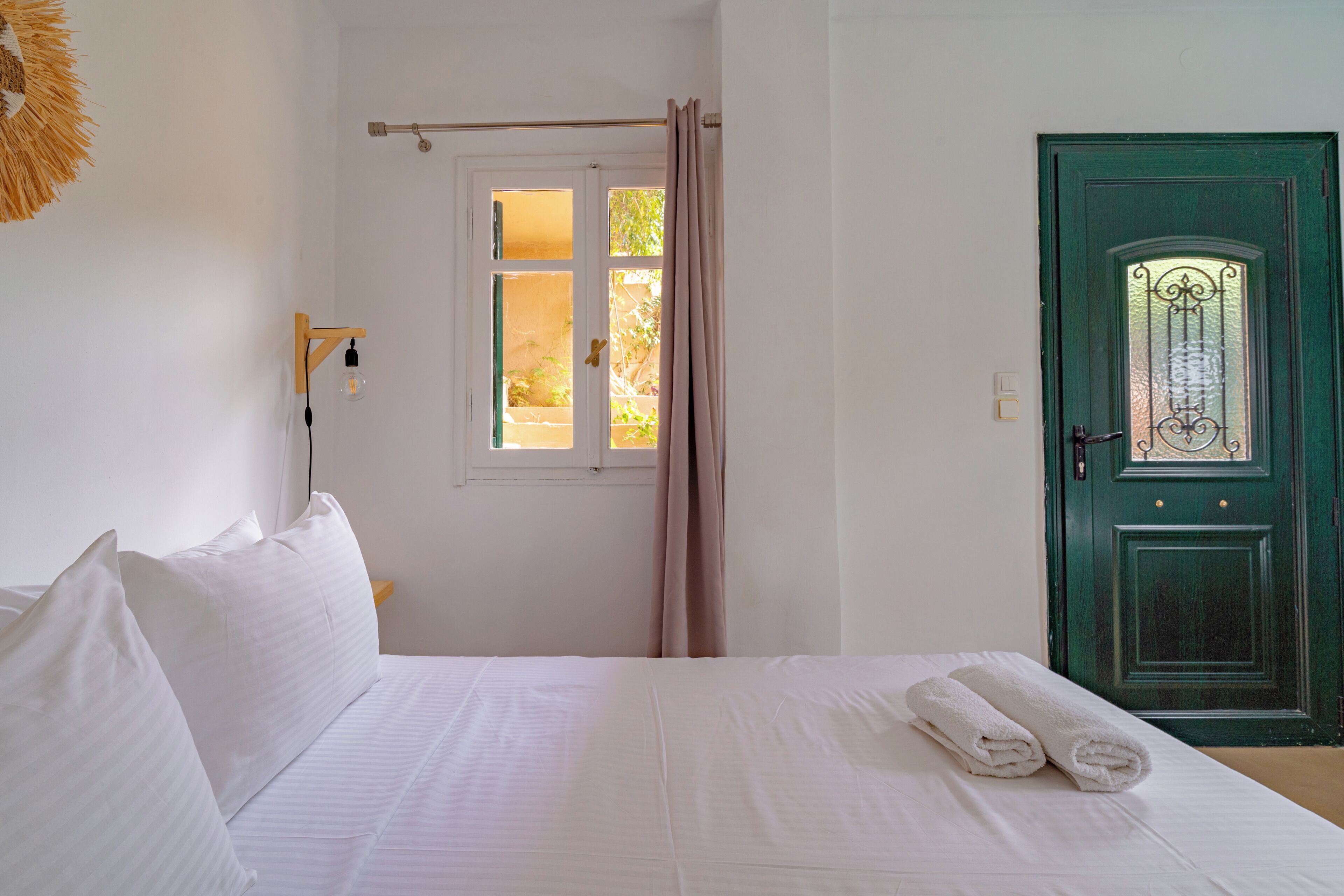 Ein Hotelzimmer mit Bett, einem Vorhangfenster, einer grünen Tür und einer Wandleuchte.