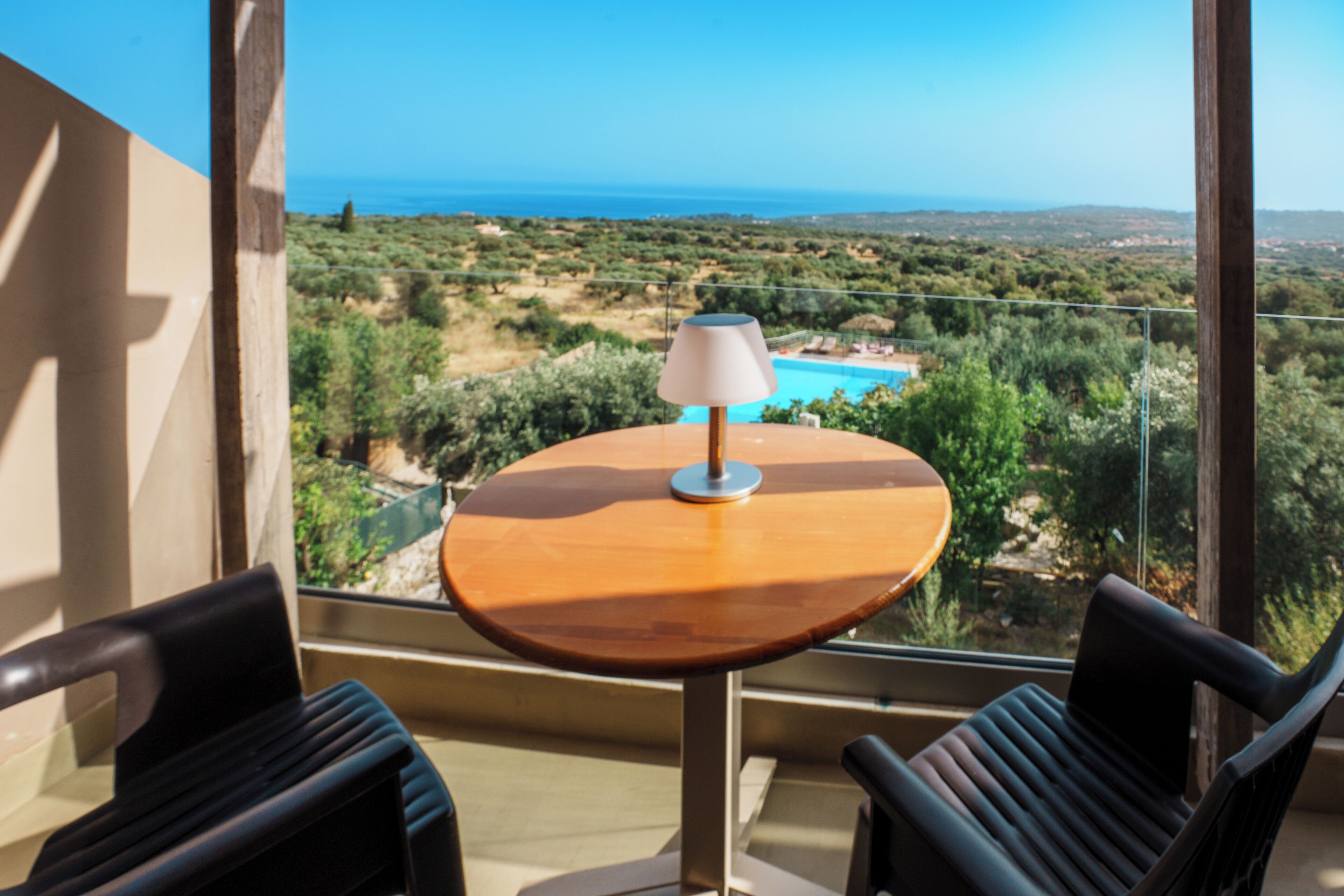 Un balcon avec une table et deux chaises, donnant sur une piscine et un paysage pittoresque.