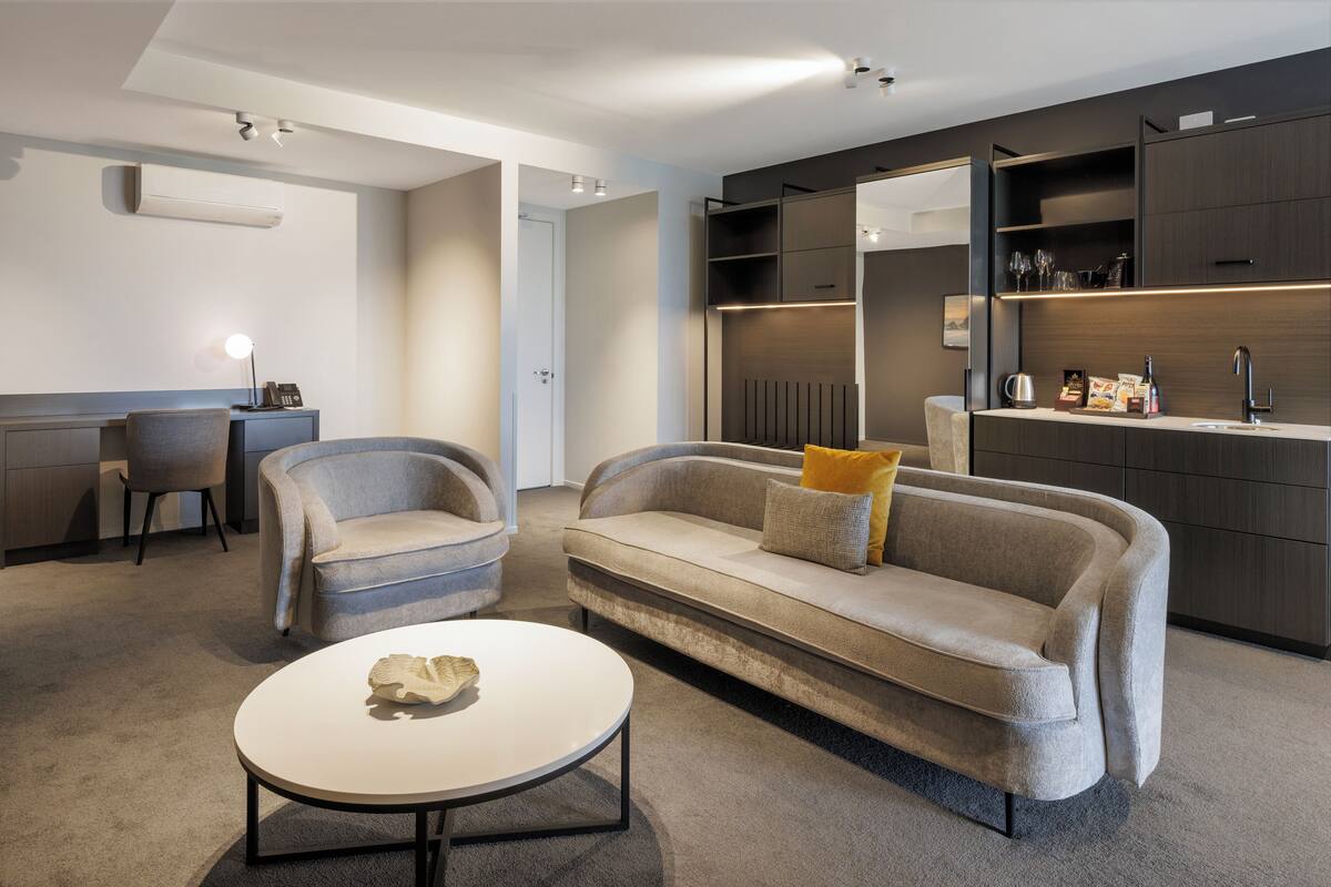 A modern living room with a sofa, two armchairs, a coffee table, and built-in shelving with decorative items.