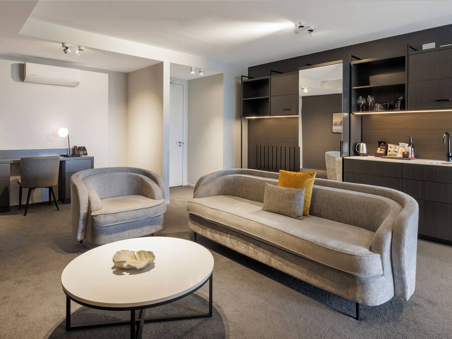 Una sala de estar moderna con un sofá, dos sillones, una mesa de centro y estanterías empotradas con objetos decorativos.