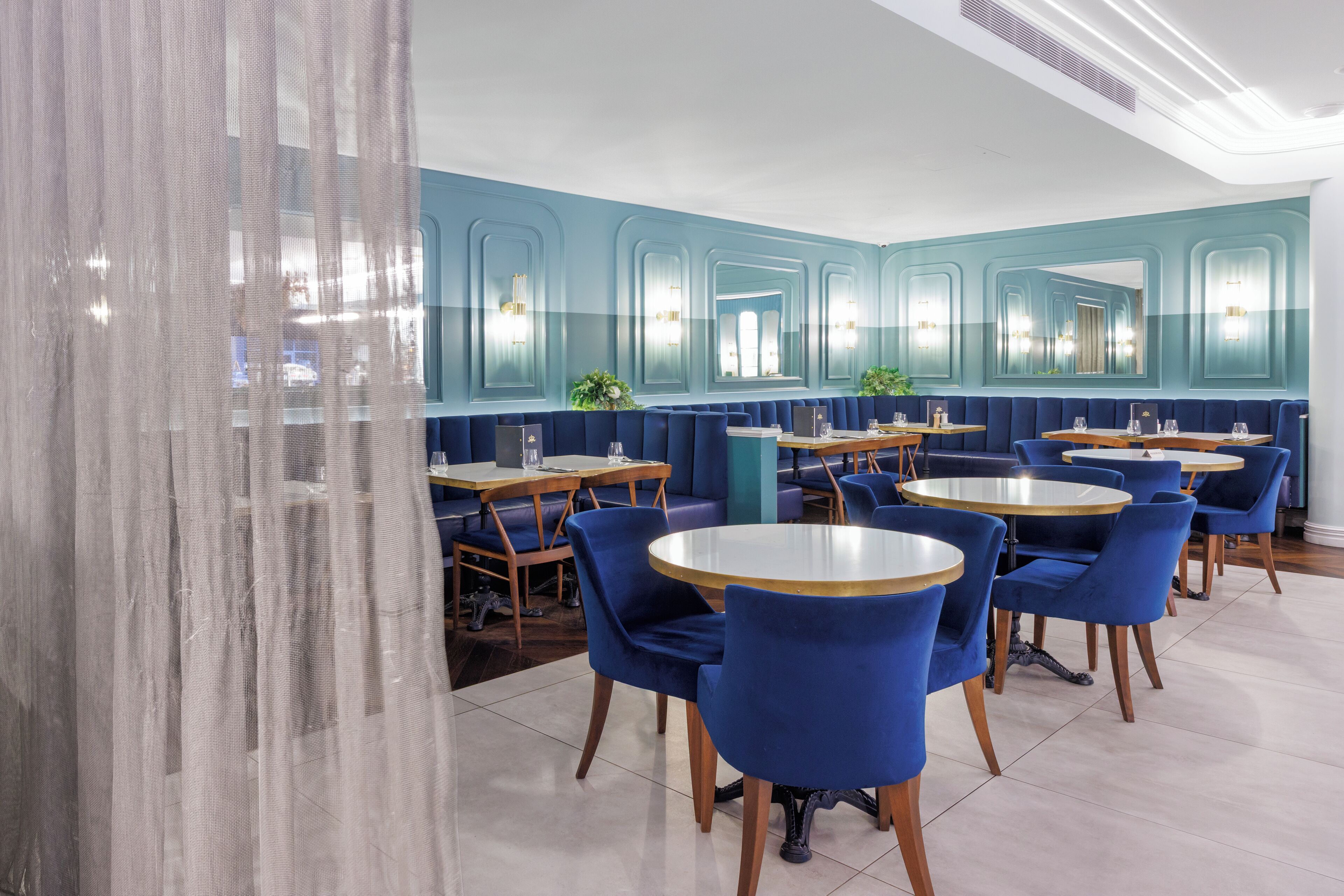 A restaurant with blue booths and round tables, featuring a modern design with teal walls and mirrored panels.