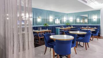 A restaurant with blue booths and round tables, featuring a modern design with teal walls and mirrored panels.