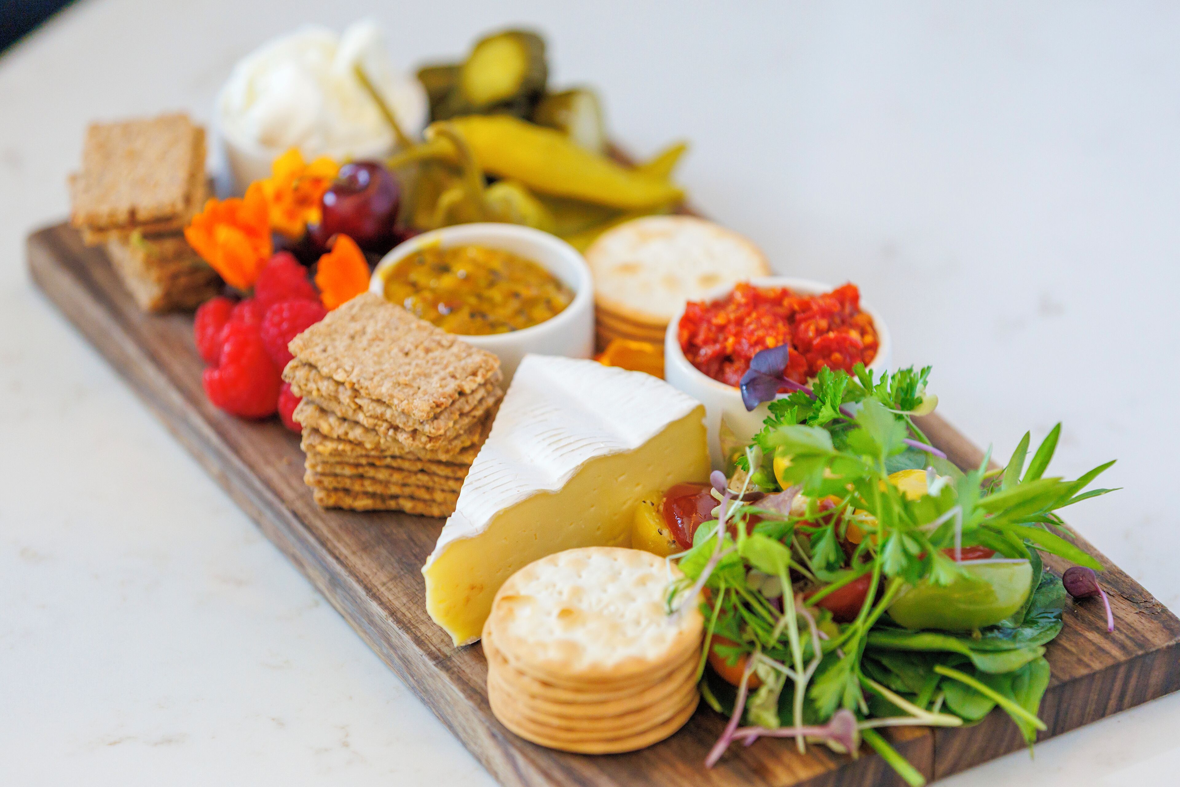 Une planche en bois garnie de différents fromages, de crackers, de cornichons et d’une salade.
