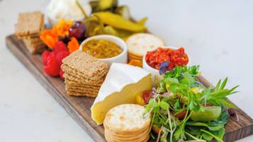 Une planche en bois garnie de différents fromages, de crackers, de cornichons et d’une salade.