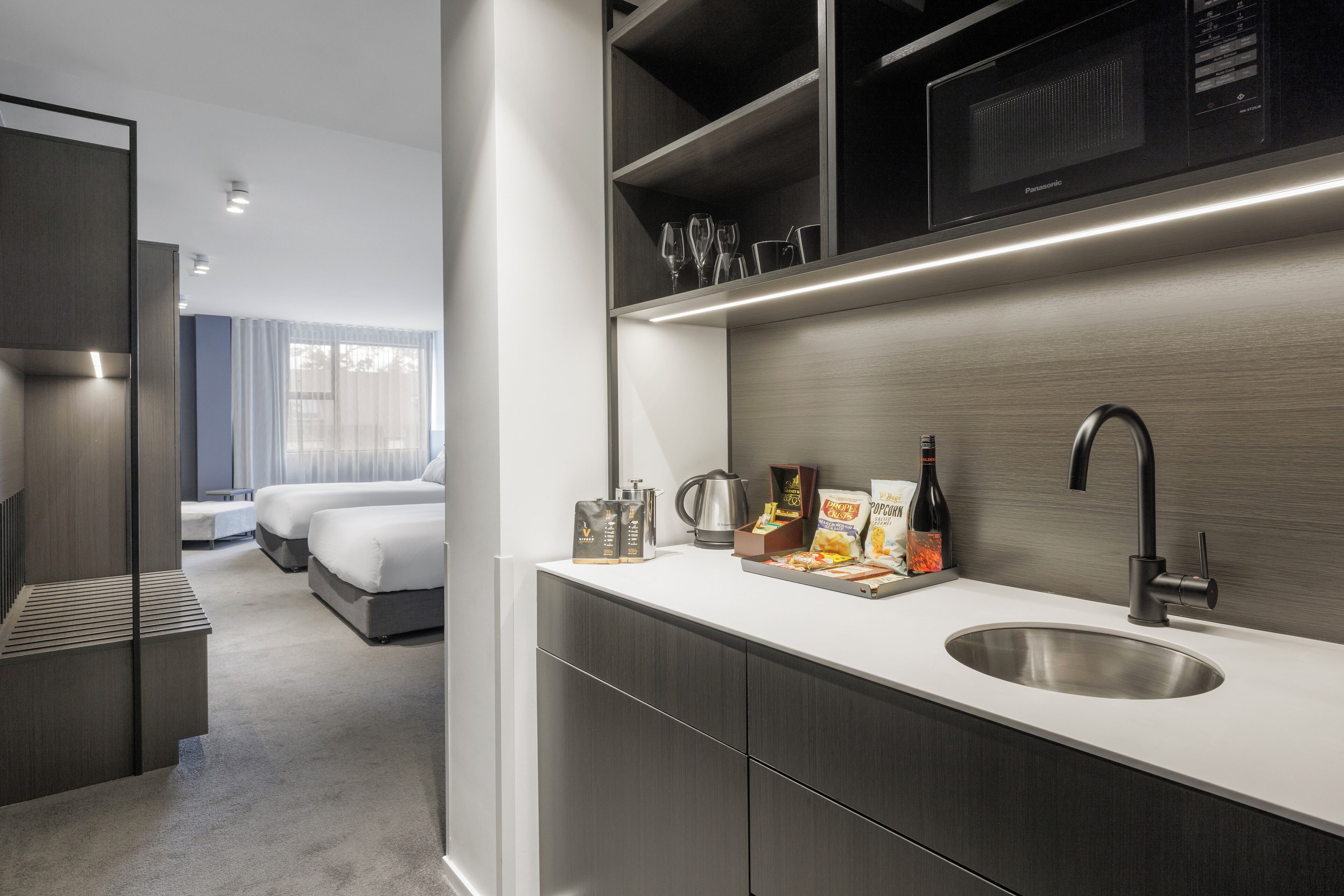 A modern hotel room with a kitchenette, a bed, and a view of the outdoors.