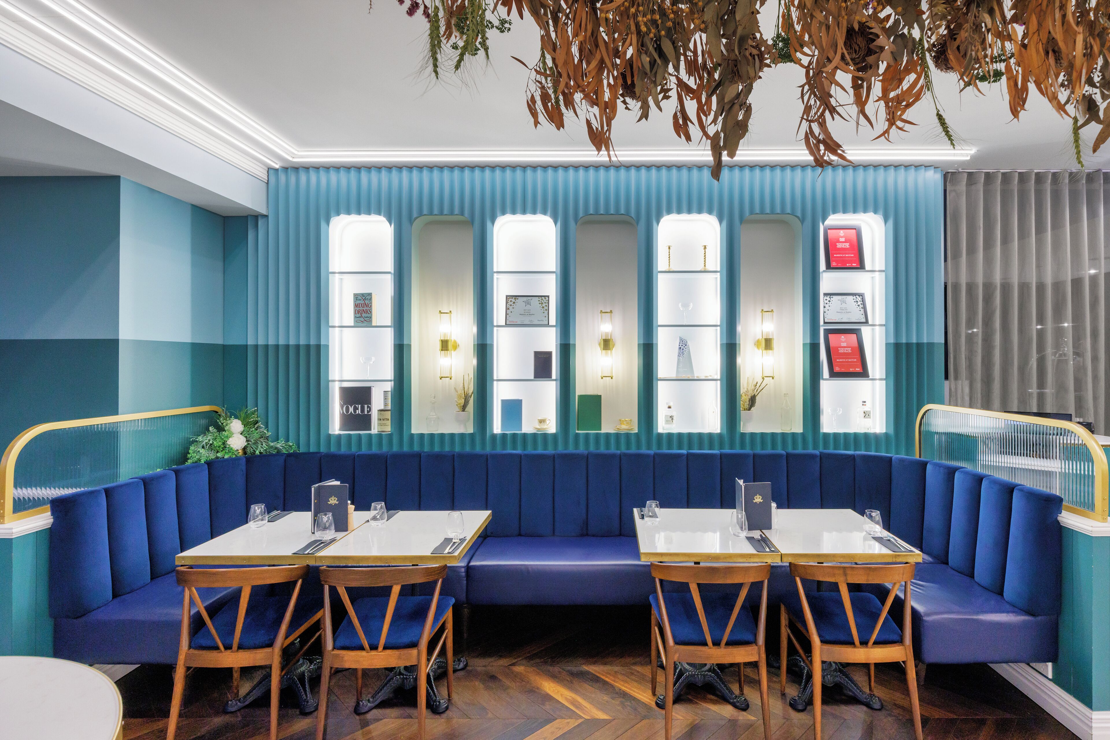 A restaurant with blue upholstered booths, wooden tables, and a wall of decorative glass panels.