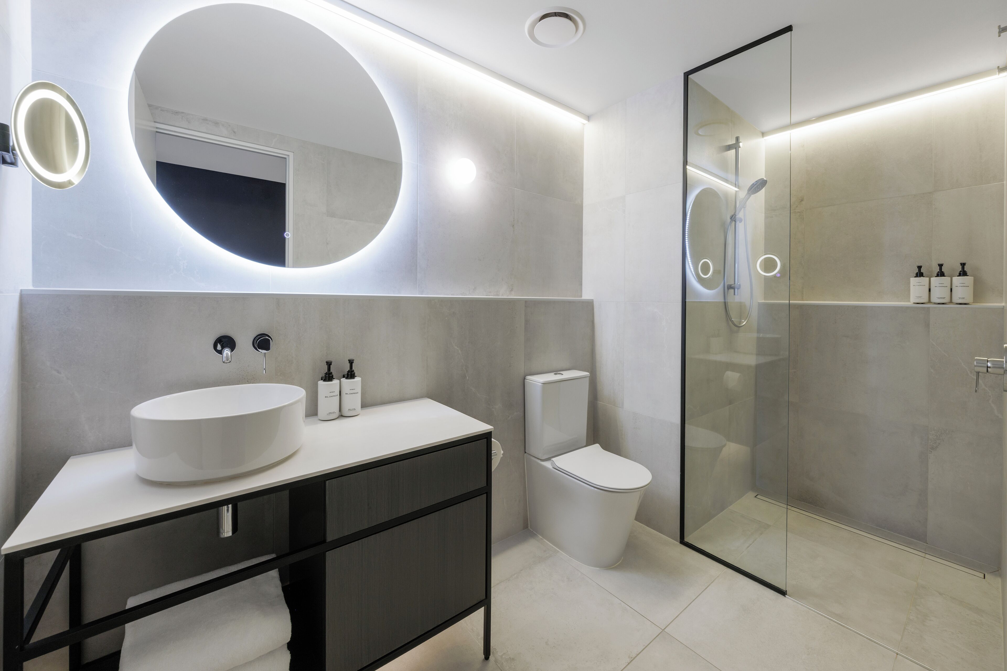 A modern bathroom with a round mirror, a white sink, a toilet, and a glass-enclosed shower area.