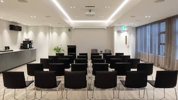 A conference room with rows of black chairs, a kitchen area, and a large window with curtains.