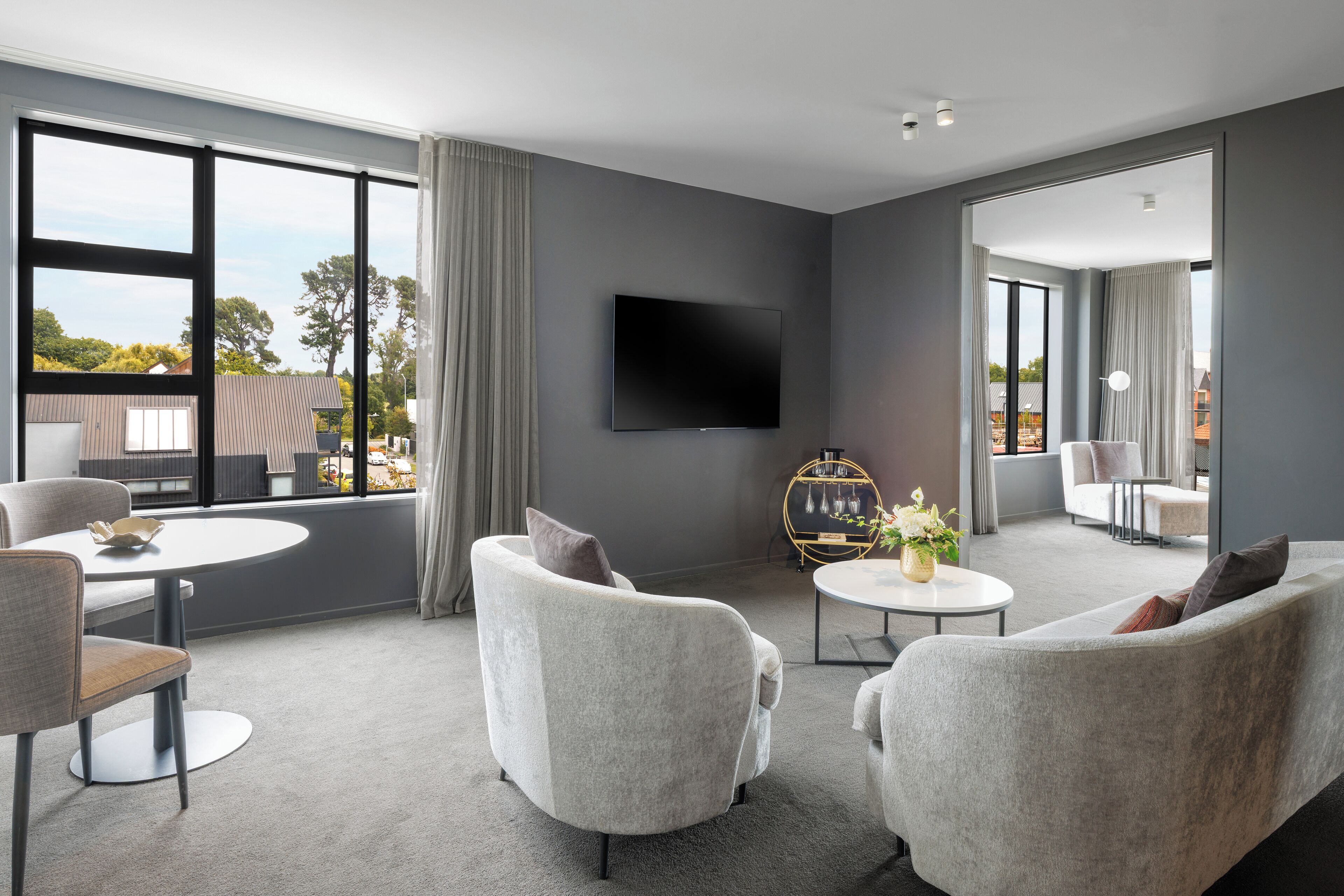 A modern living room with a flat-screen TV, grey sofas, a round coffee table, and a view of the outdoors.