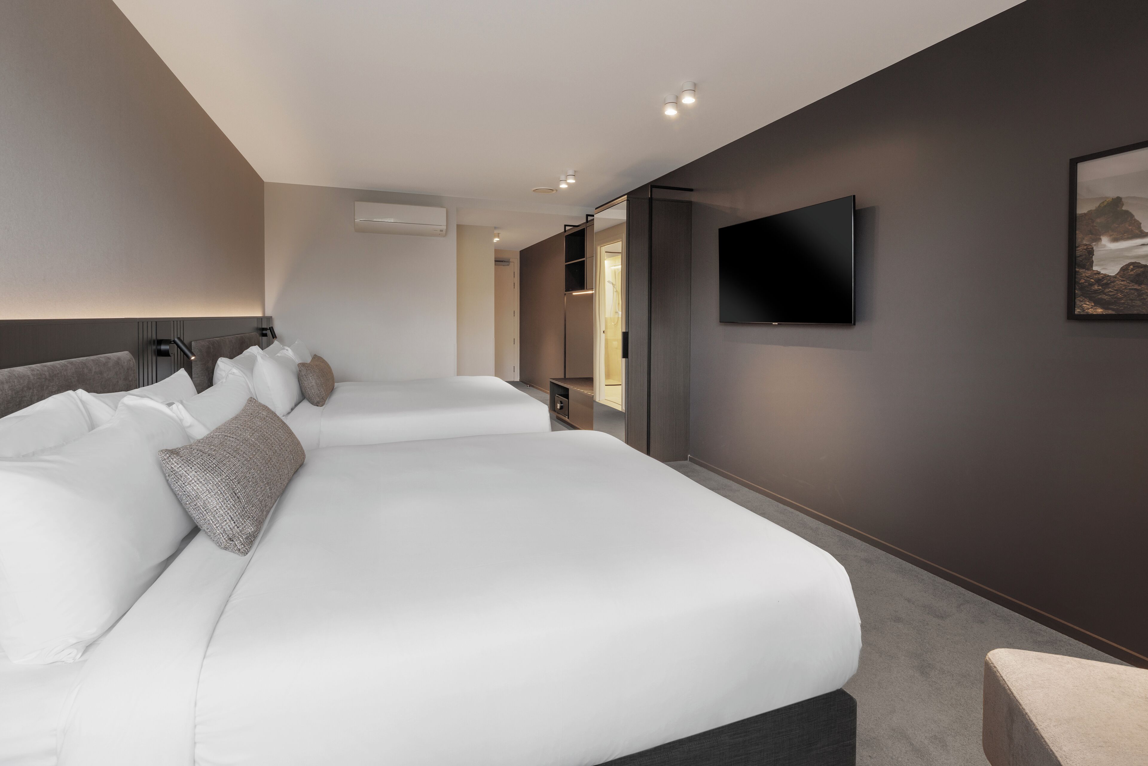 Une chambre d’hôtel moderne avec deux lits, un téléviseur à écran plat fixé au mur et une grande fenêtre donnant sur l’extérieur.