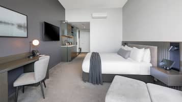 Una habitación de hotel moderna con cama, escritorio, silla, televisor y una kitchenette pequeña.