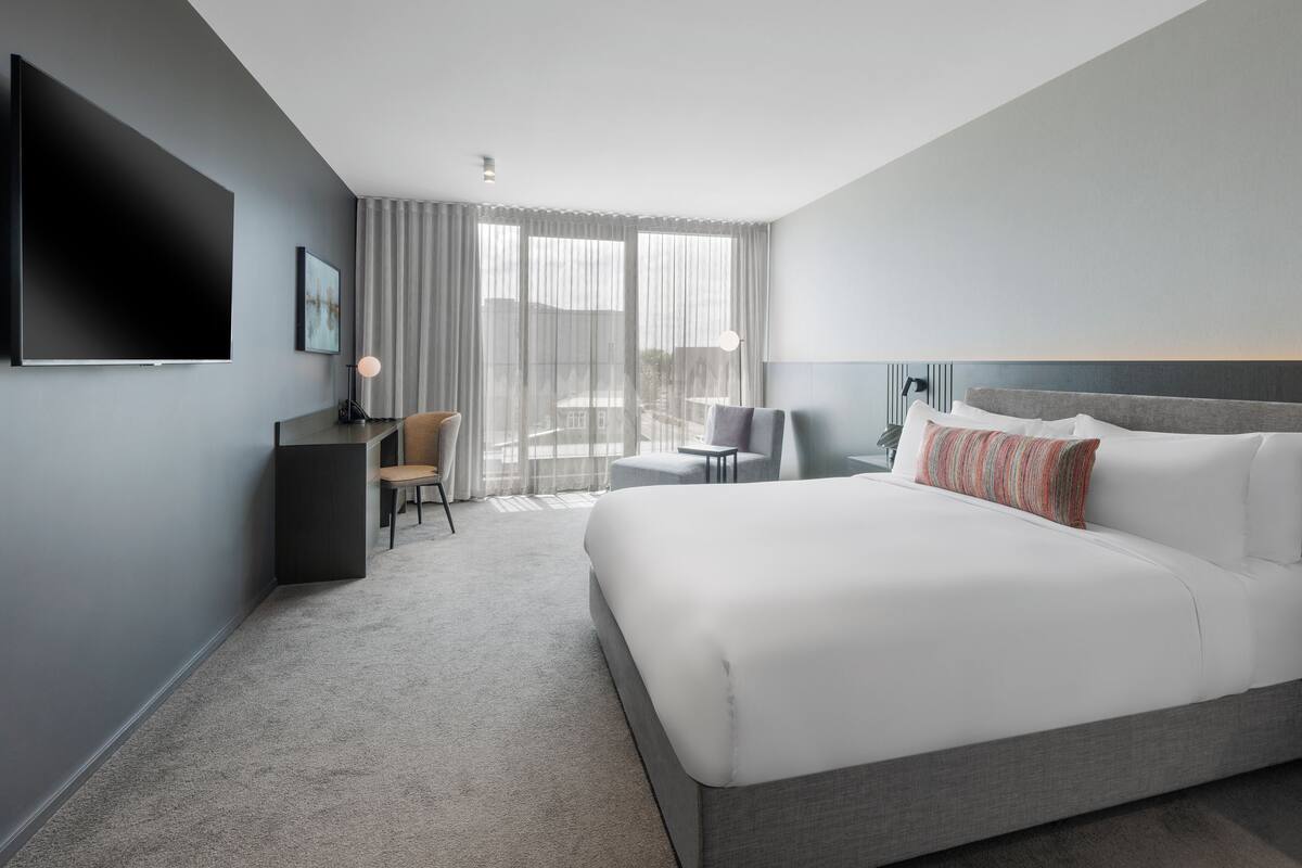 A modern hotel room with a large bed, a desk, a chair, and a TV.