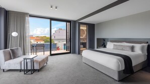 A modern hotel room with a large bed, a sofa, a small table, and a view of the city through large windows. - The Mayfair (Christchurch)