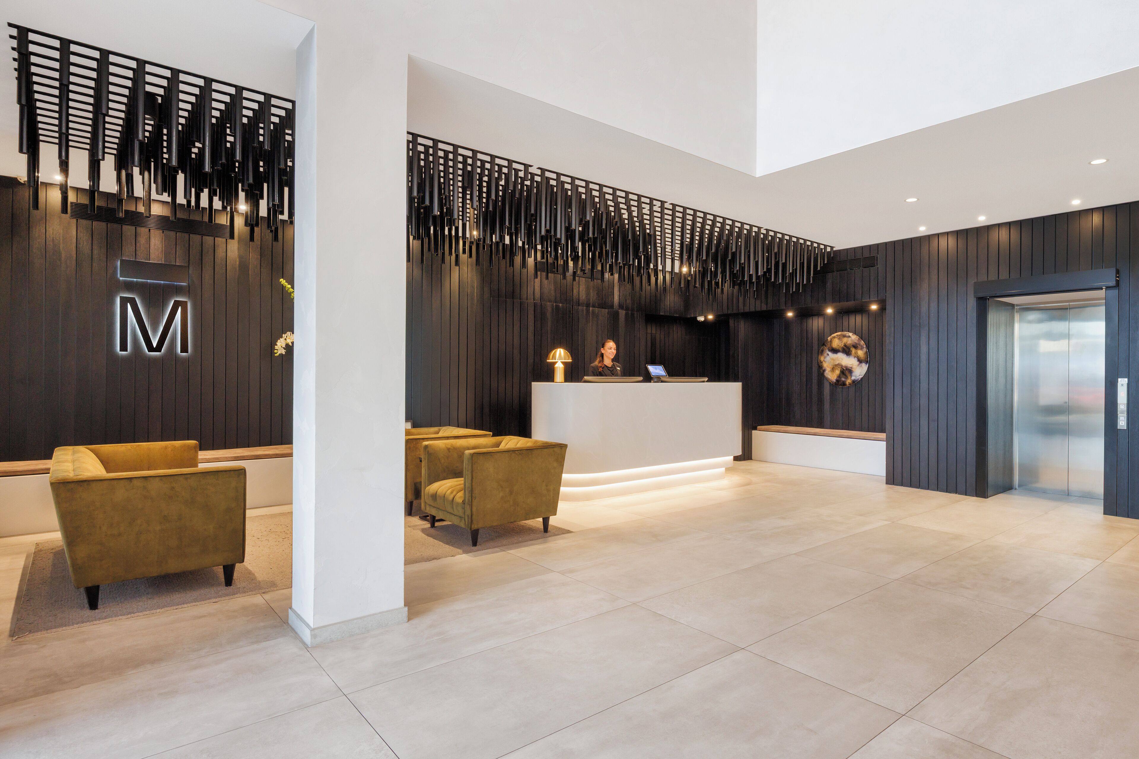 A modern reception area with a reception desk, two sofas, and a decorative wall with a 'M' sign.