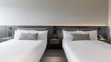 A modern hotel room with two beds, a bedside table with a lamp, and a small nightstand with a phone.