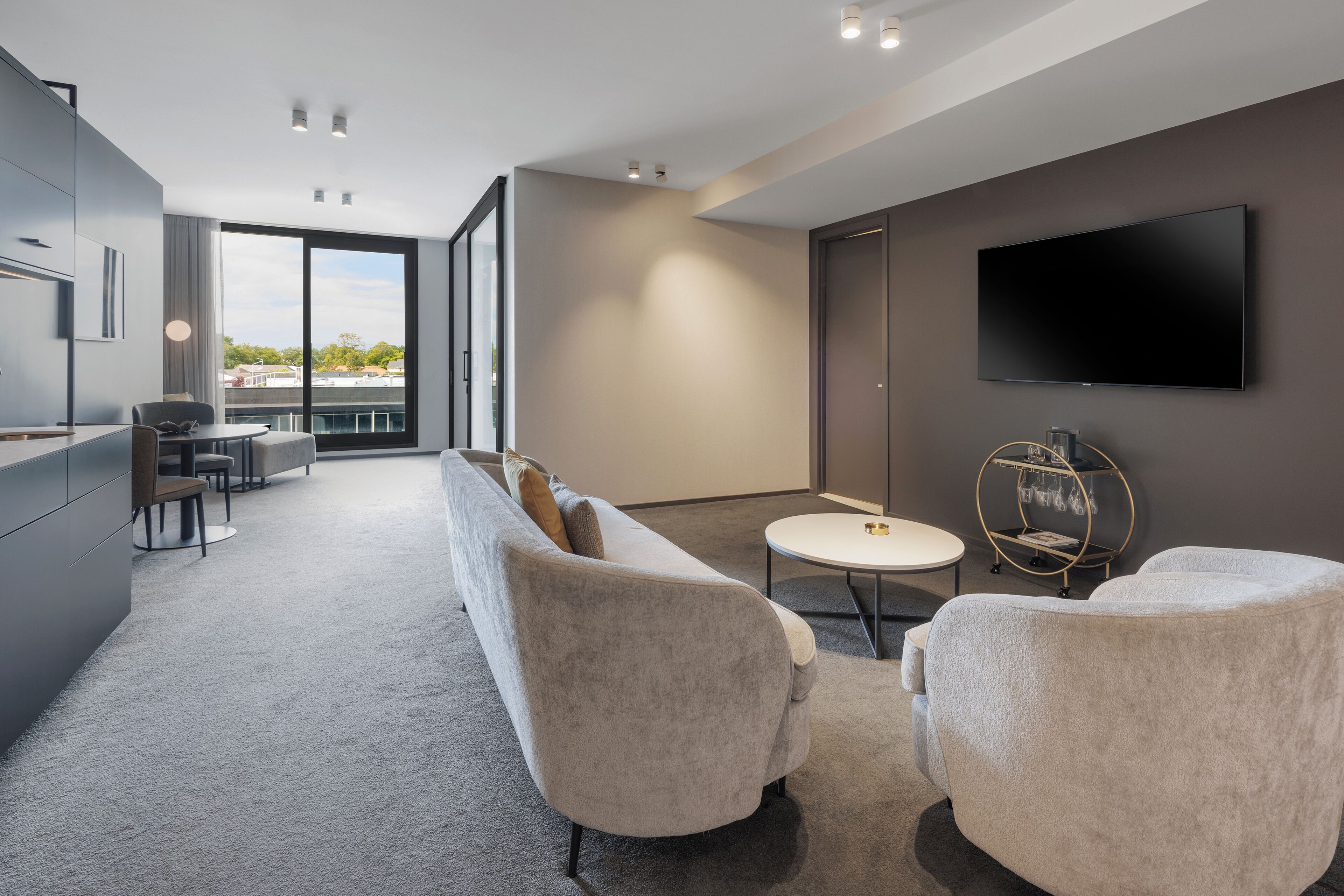 Un salon moderne avec un canapé gris, une table basse ronde et un téléviseur à écran plat fixé au mur.