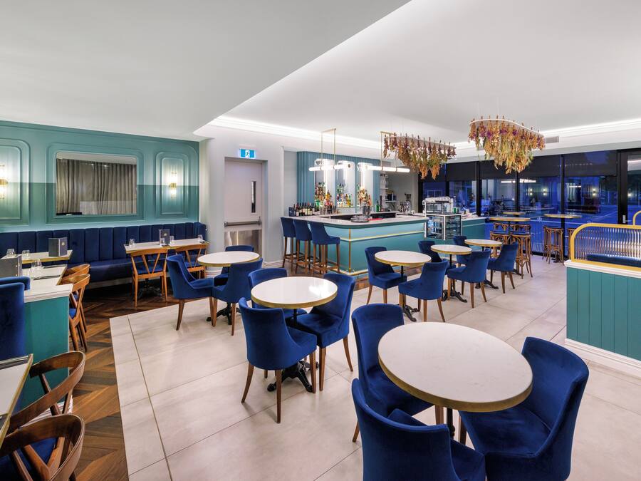 Un restaurant moderne avec des sièges bleus, des tables rondes et un espace bar.
